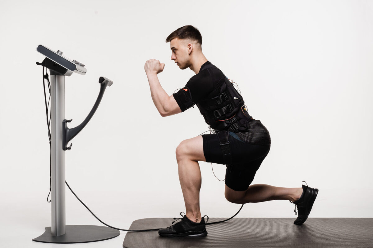 Man performing a lunge exercise while wearing an EMS (Electrical Muscle Stimulation) suit, connected to a control unit.